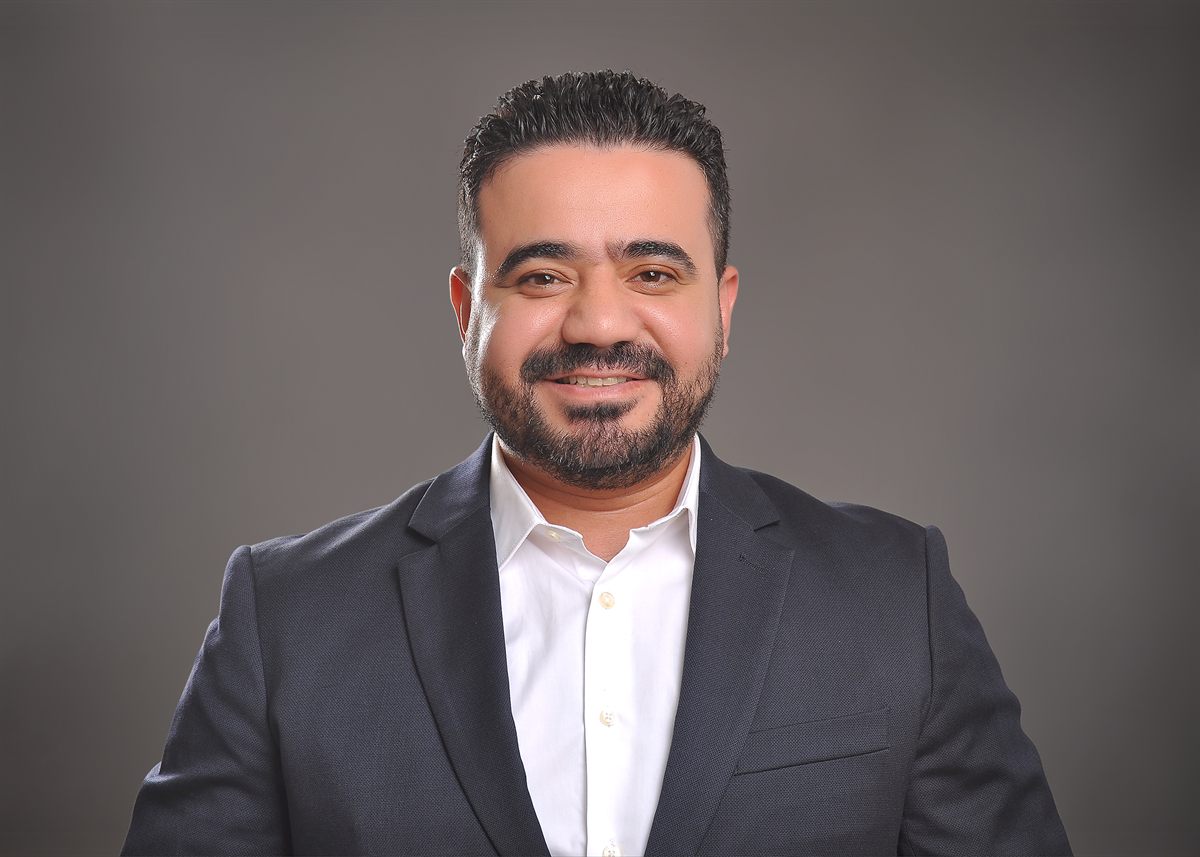 Amr Samir smiling, in a dark suit